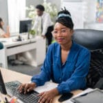 Polite, elegant customer service representative in large corporation sits at computer, tapping fingers on keyboard, surfing Internet, preparing documentation, filling out reports, making appointments